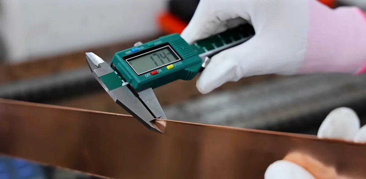 Digital caliper measuring the thickness of a copper component